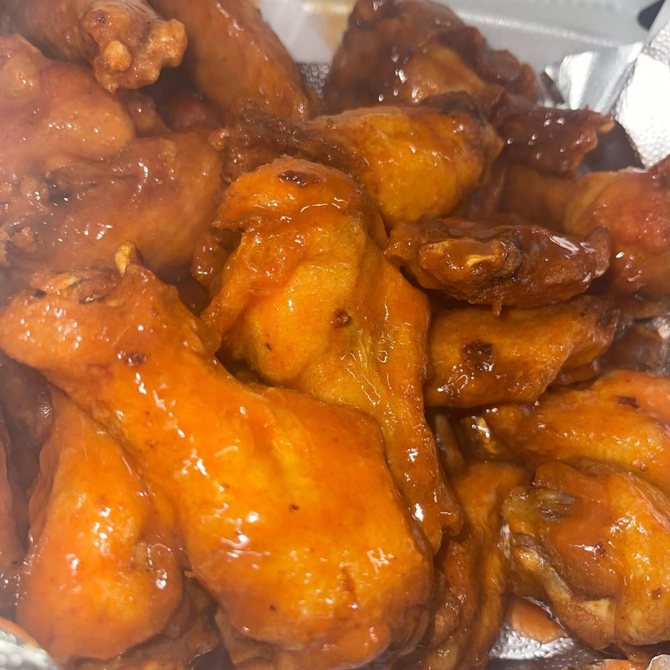 Close-up of Super Fratelli's Pizza's chicken wings, coated in a glistening orange-brown sauce.