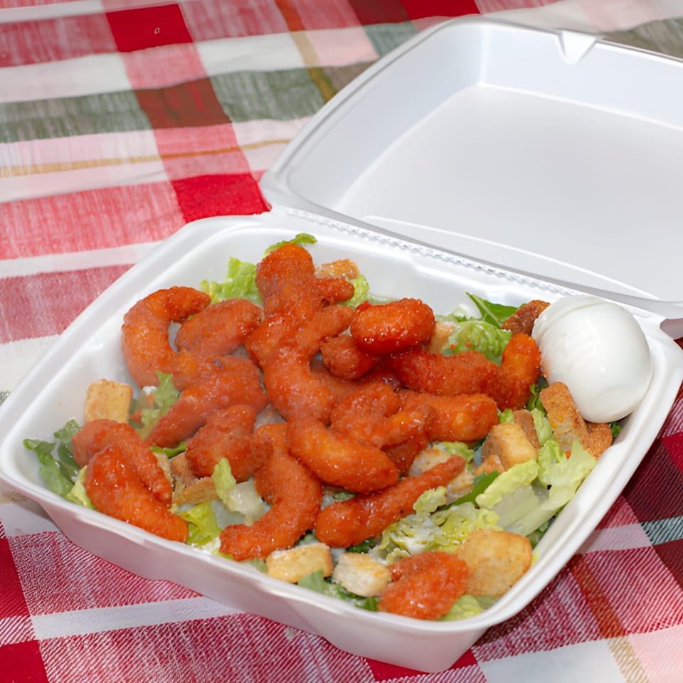Buffalo chicken salad with lettuce, croutons, and a hard-boiled egg in a takeout container.