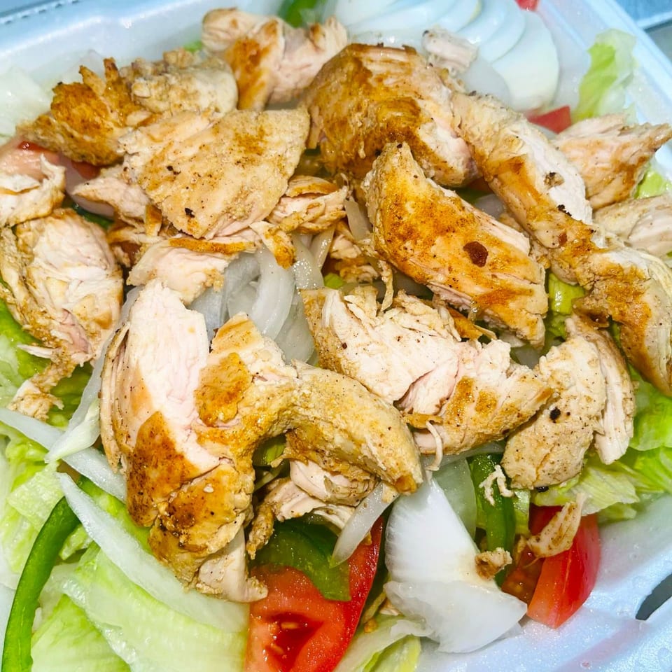 Grilled chicken salad with lettuce, tomatoes, onions, and green peppers in a white container.