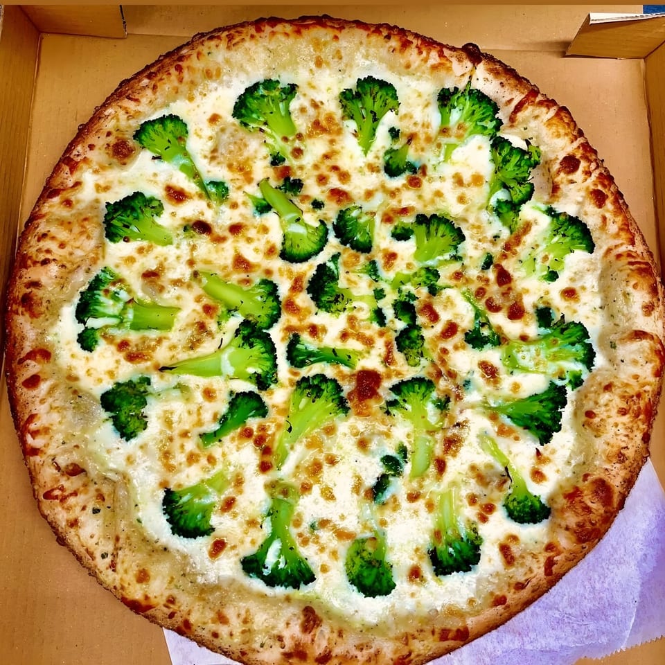 A whole Super Fratelli's white pizza with broccoli florets and melted cheese in a cardboard box.