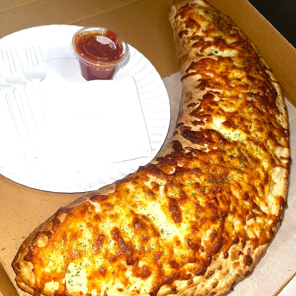A large, golden-brown Super Fratelli's calzone with melted cheese and herbs, next to a plate with sauce.